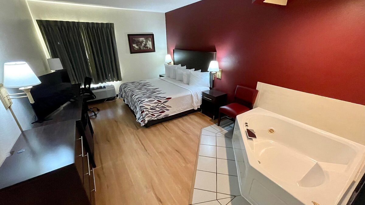 Hotel room interior featuring a large bed, desk, and an in-room hot tub positioned beside the sleeping area